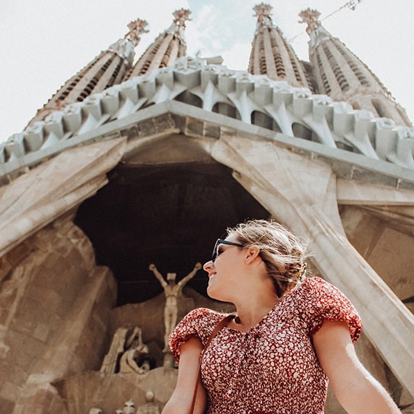 Worm's eye view of a Fairfield student looking up whimsically while standing under the entrance to the Sagrada Família Basílica.